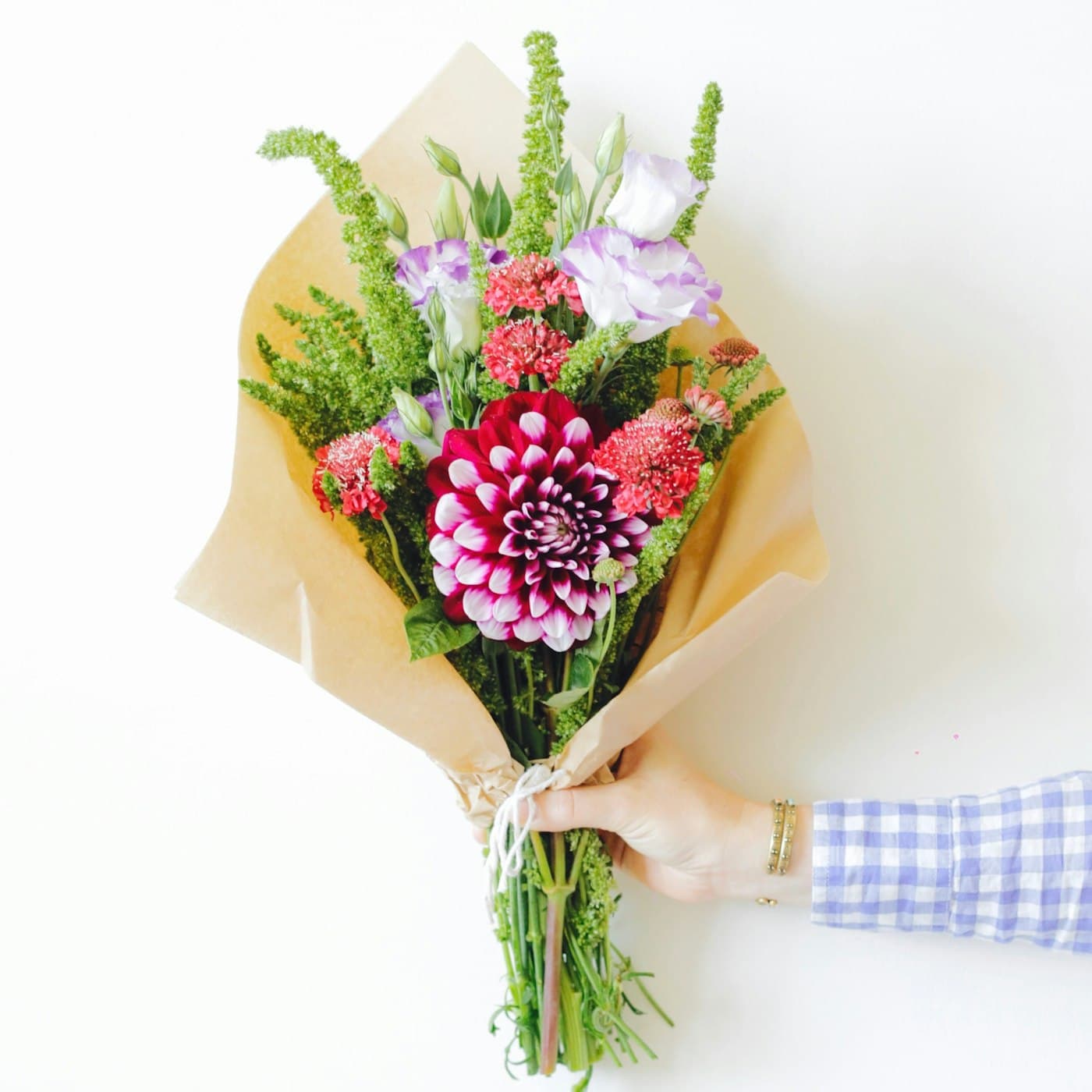 Bouquet champêtre coloré tenu à la main dans un papier kraft